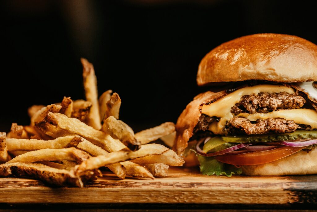 A close up of a stacked burger and a pile of golden fries against a black background.