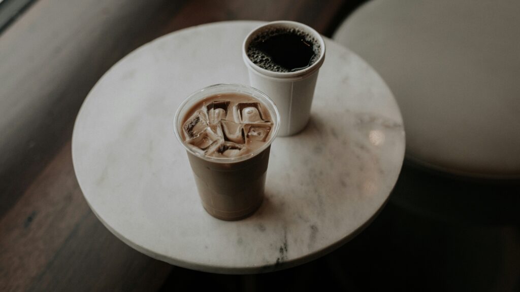 Two takeaway iced coffee cups on a round marble table, seen from above.