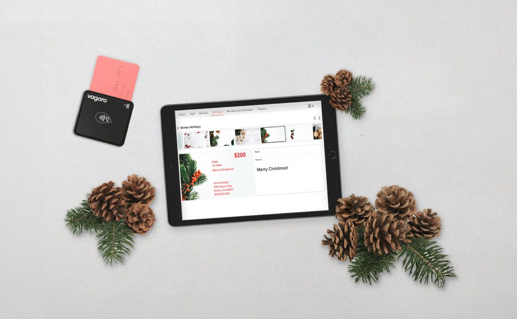 A tablet showing an online store beside a card reader and pine cones on a pale surface.