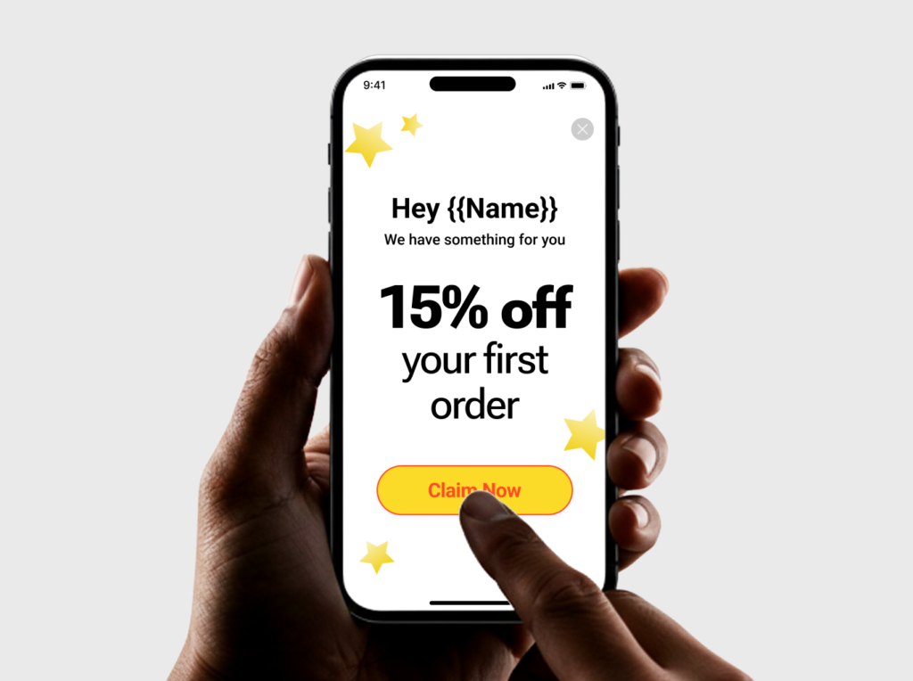 A hand holds a phone showing a promotional message that opens with Hey followed by an unrendered name placeholder, above a 15 percent off your first order offer and a Claim Now button.
