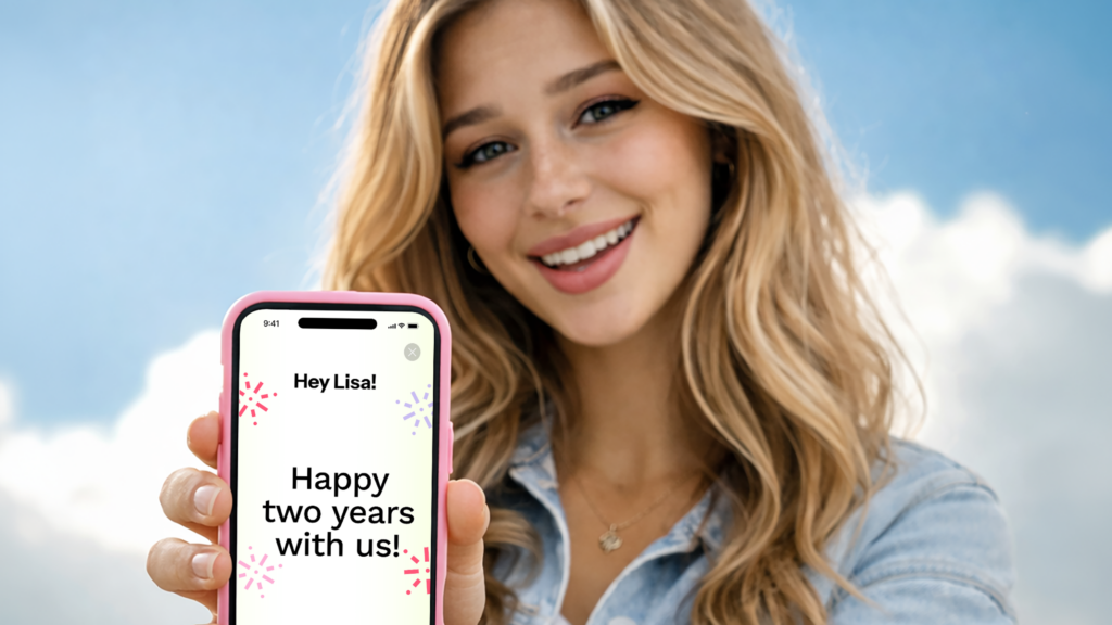 Young woman outdoors holding up a phone that plays a frame reading Hey Lisa, happy two years with us.