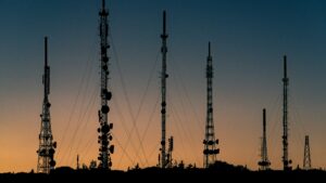 Silhouettes of several lattice telecommunications towers against an orange and blue dusk sky.